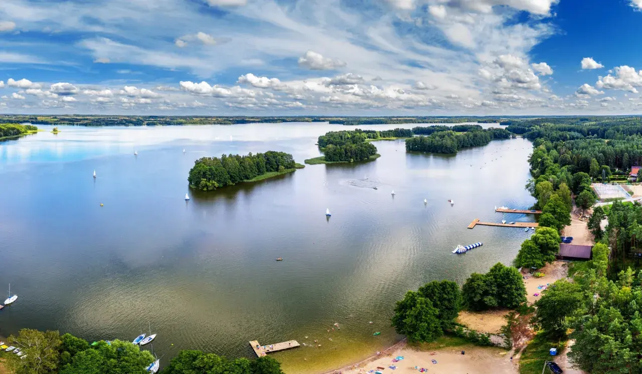 Malownicze zalewy w Polsce z żaglówkami, wyspami i plażą pełną wypoczywających ludzi.