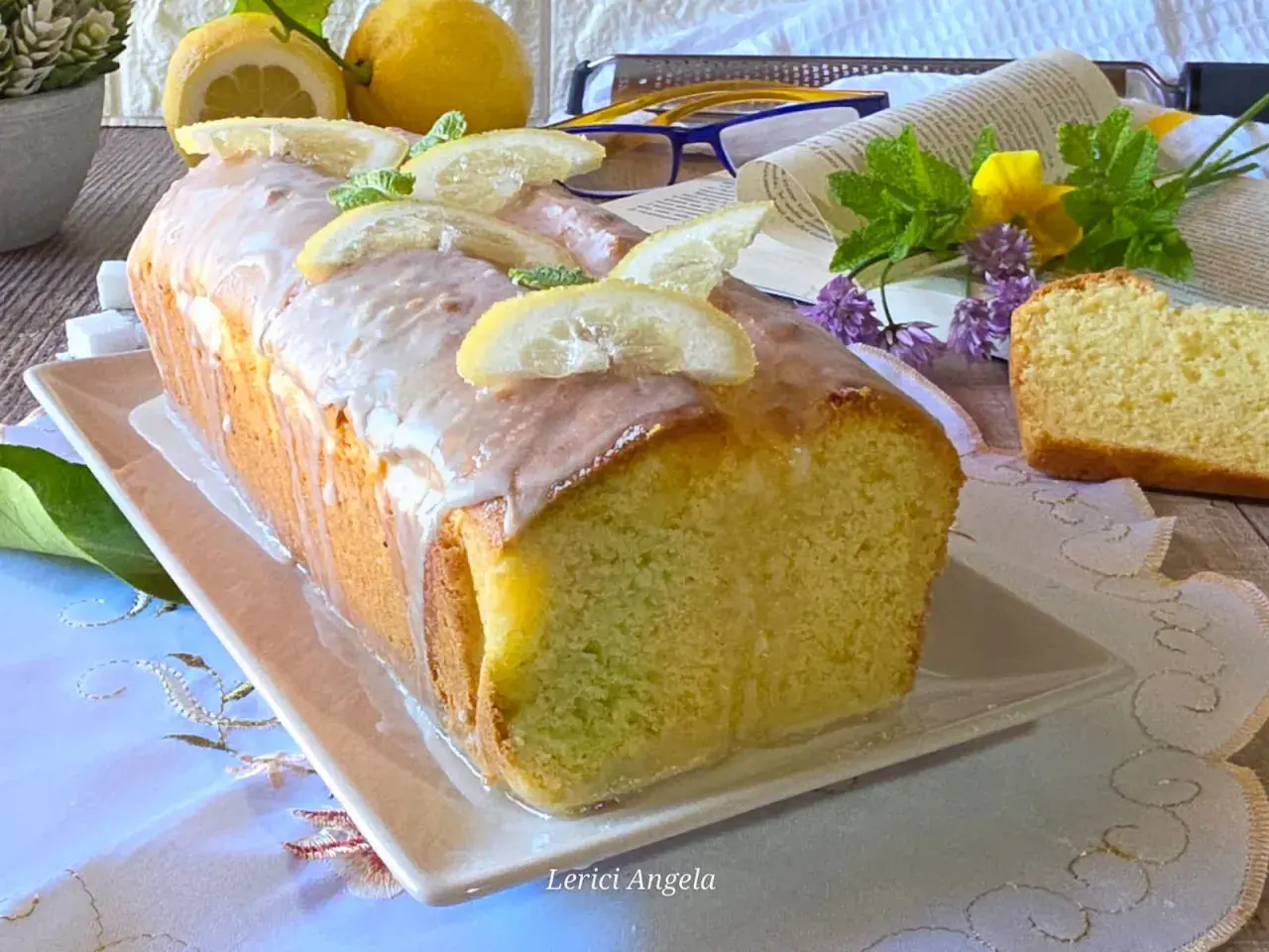 Un delizioso plumcake al limone glassato, decorato con fette di limone e menta, pronto per essere gustato.