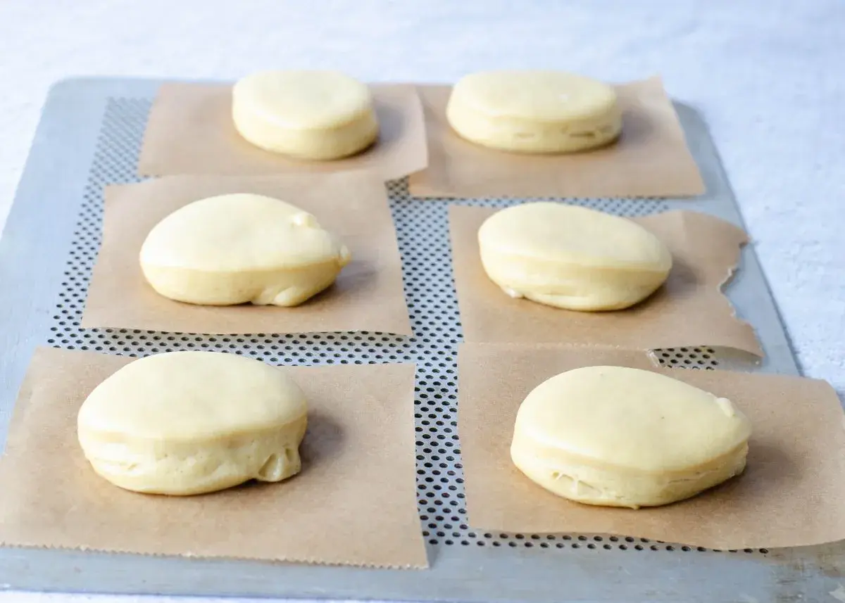 Seis bolas de fraile crudas, listas para hornear, descansan sobre papel de horno en una bandeja metálica.