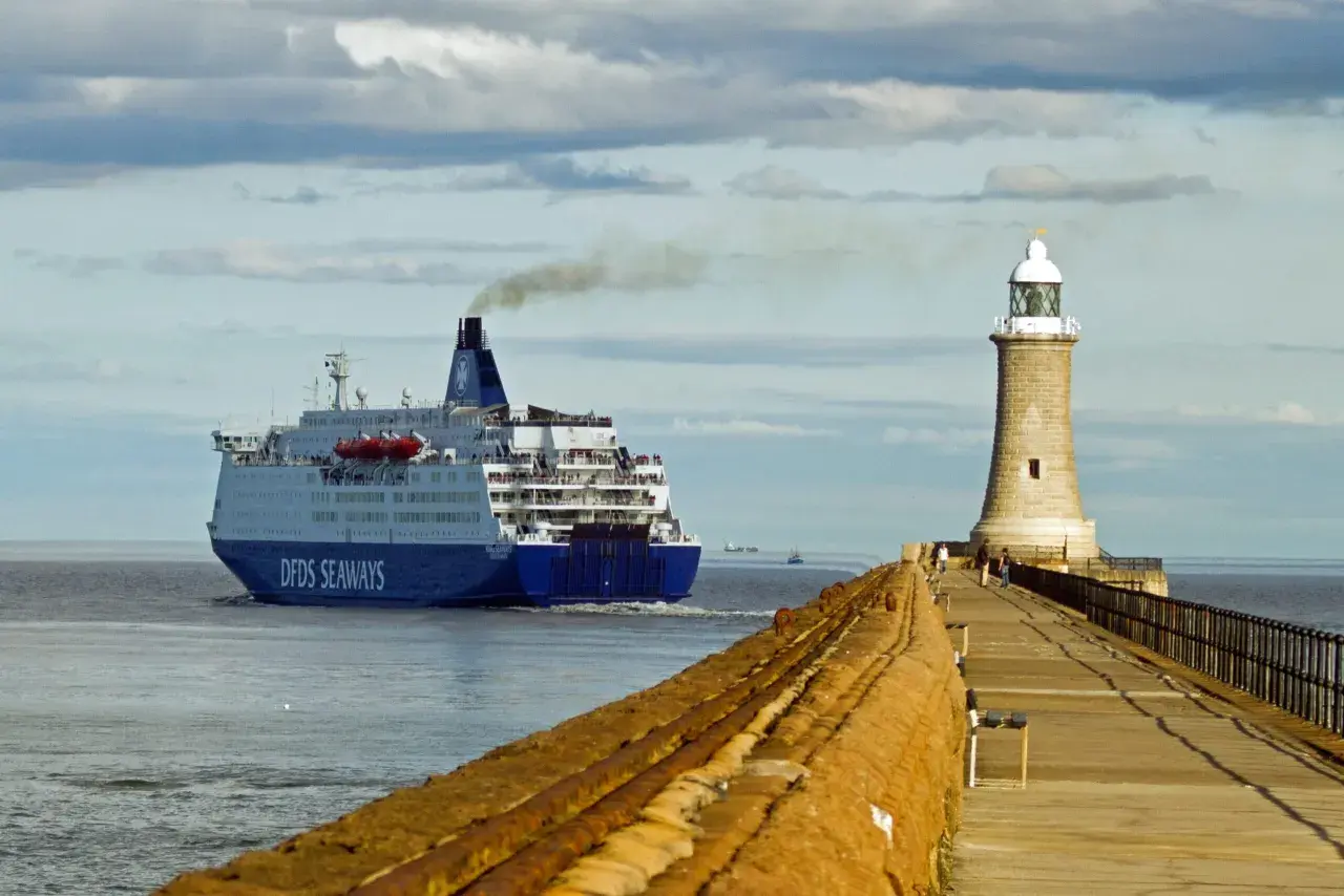 Duży prom DFDS Seaways wypływa z portu, kierując się na Bornholm. Obok stoi latarnia morska.