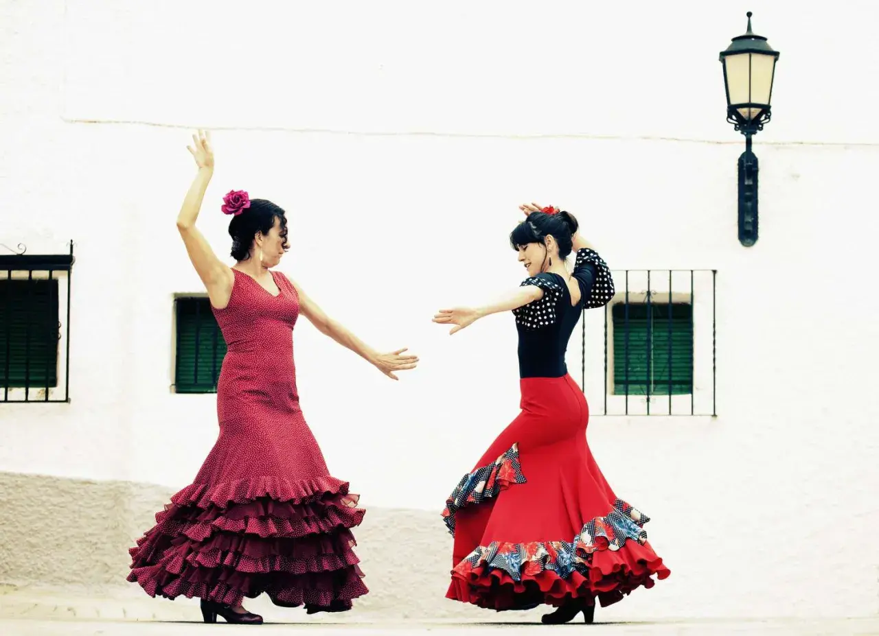 Dos mujeres bailan flamenco, con faldas rojas y volantes. Una lección de baile flamenco para principiantes.