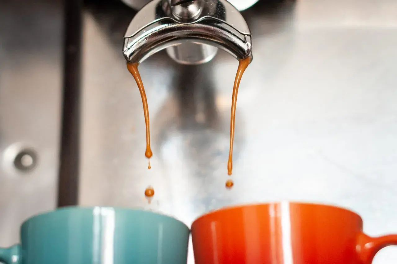 Gorące, aromatyczne espresso co to? Dwie strumienie kawy spływają do kolorowych filiżanek.