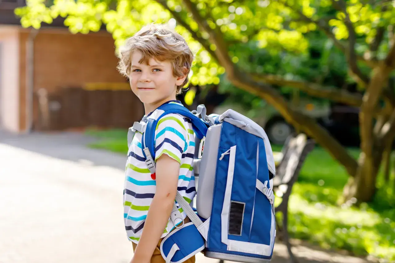 Niño sonriente con mochila azul, listo para ir al cole.