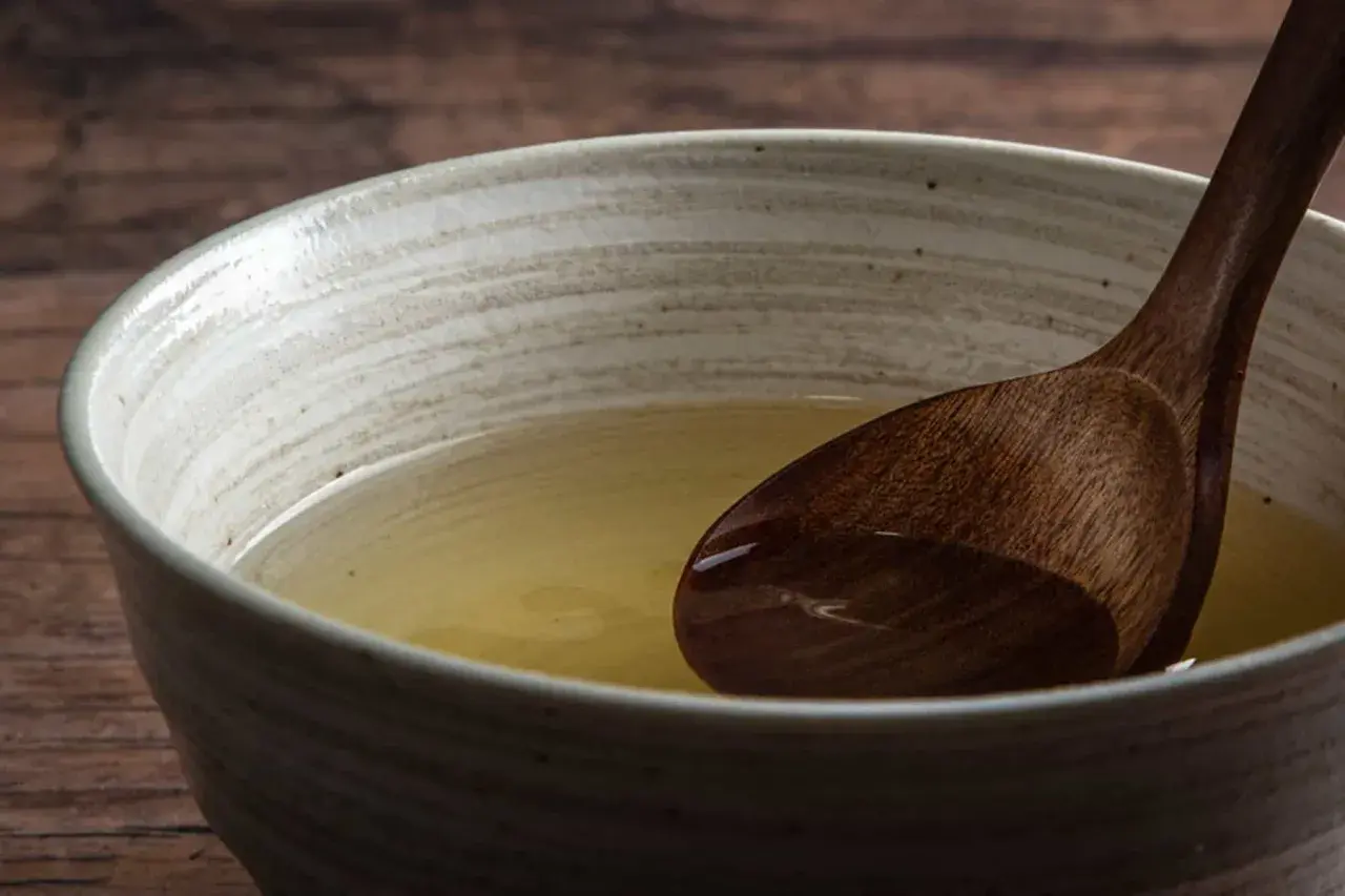 A wooden spoon rests in a bowl of clear, golden broth, hinting at the subtle flavors of various types of dashi.