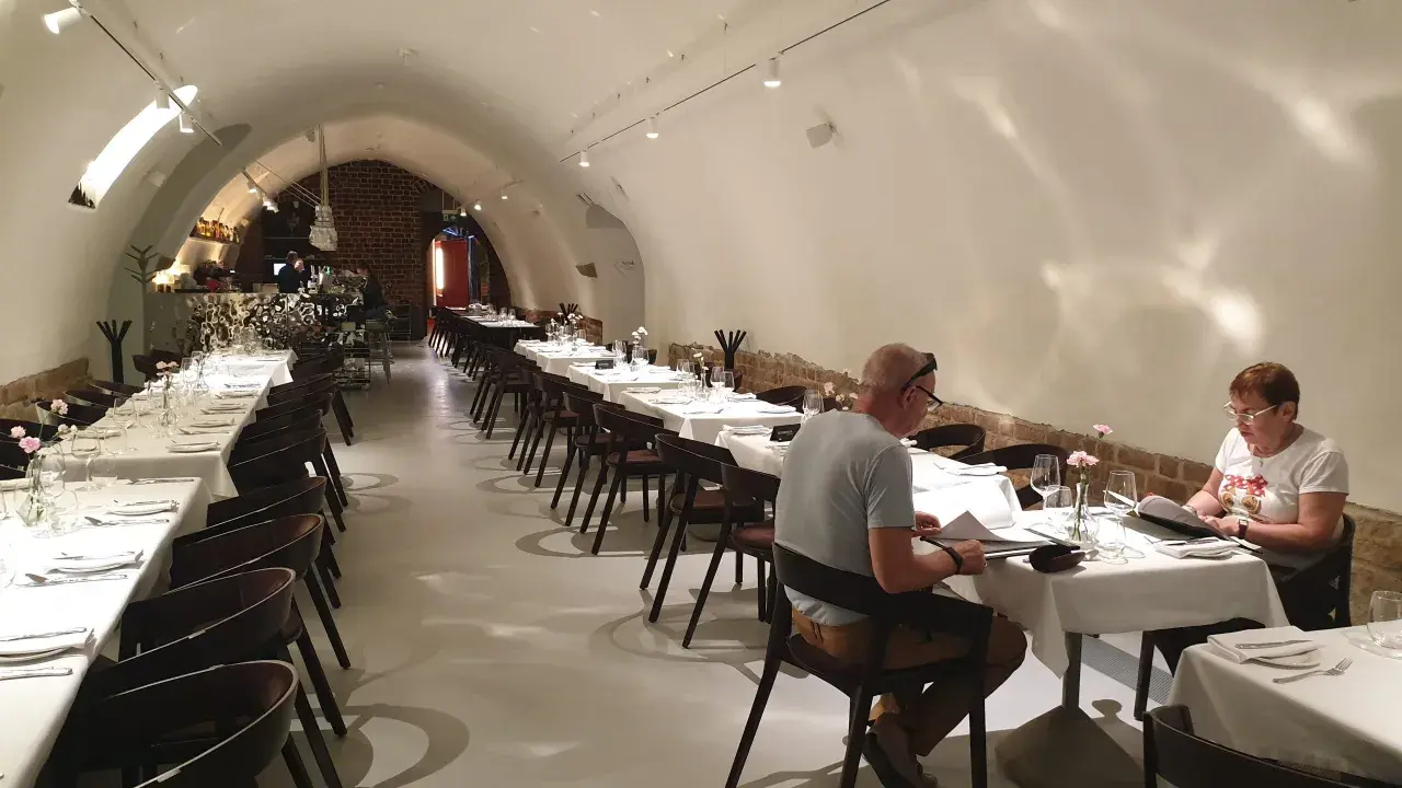 Elegancka sala restauracyjna z białymi obrusami i nakrytymi stołami. W tle bar. To może być najstarsza restauracja w Polsce.