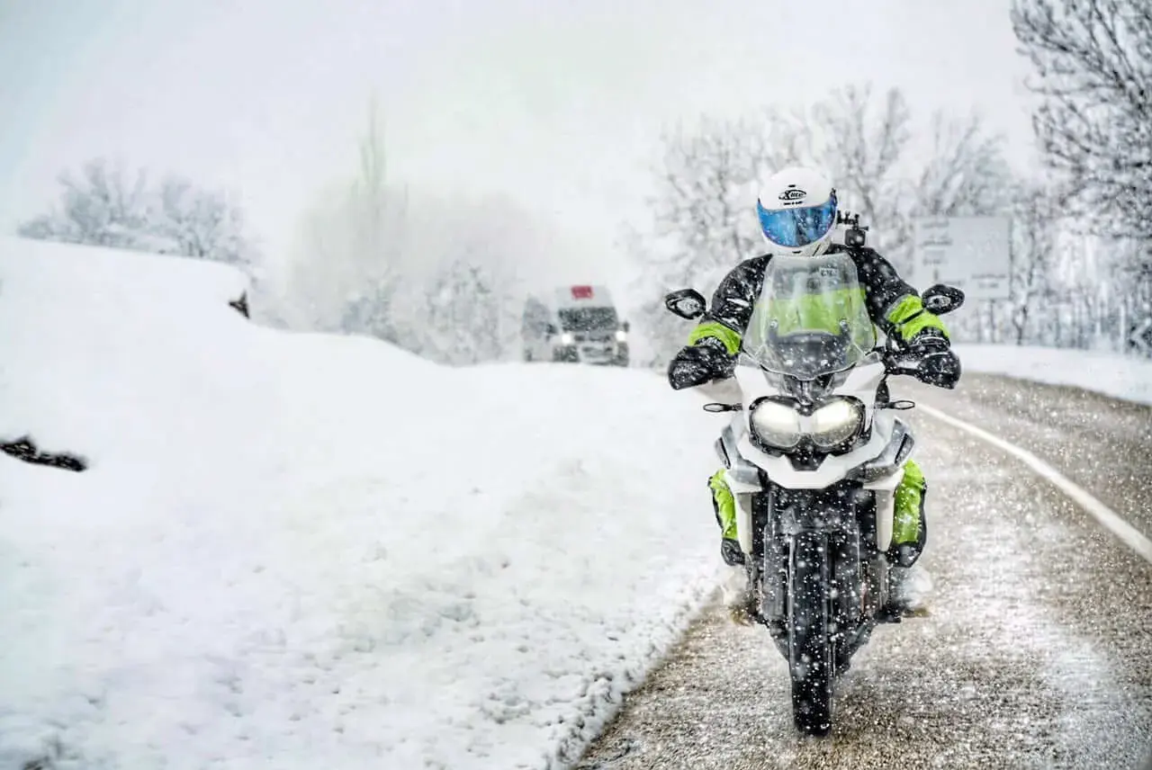 Motocyklista w kasku i zimowej odzieży jedzie po zaśnieżonej drodze.