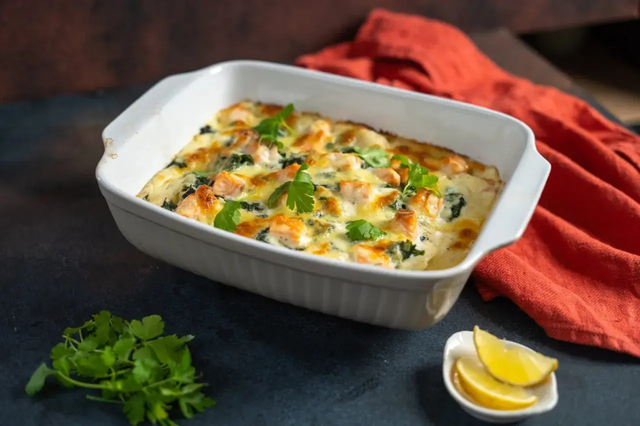 Herzhafte Lachs Spinat Lasagne, goldbraun überbacken, garniert mit frischer Petersilie. Dazu Zitronenspalten.