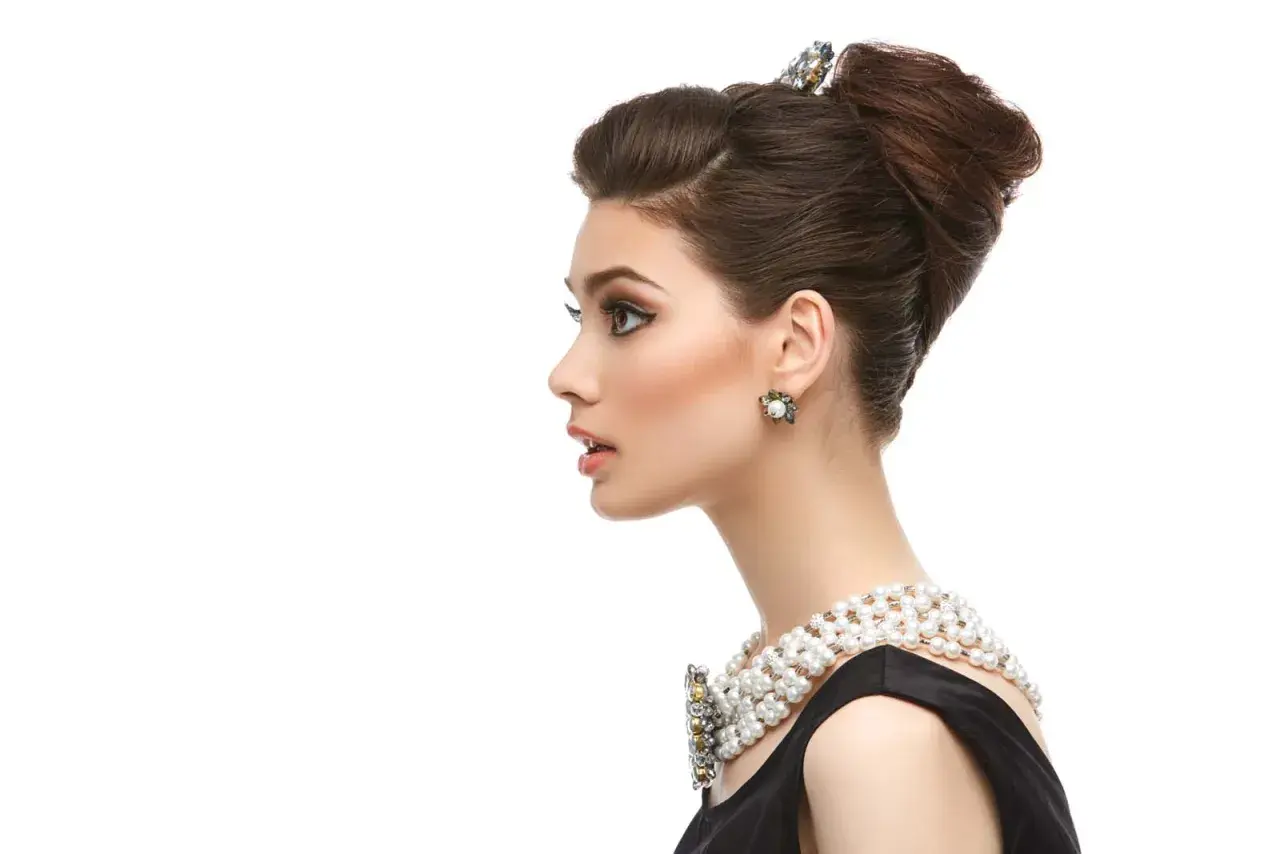 Elegante mujer con moño italiano, collar de perlas y pendientes llamativos.