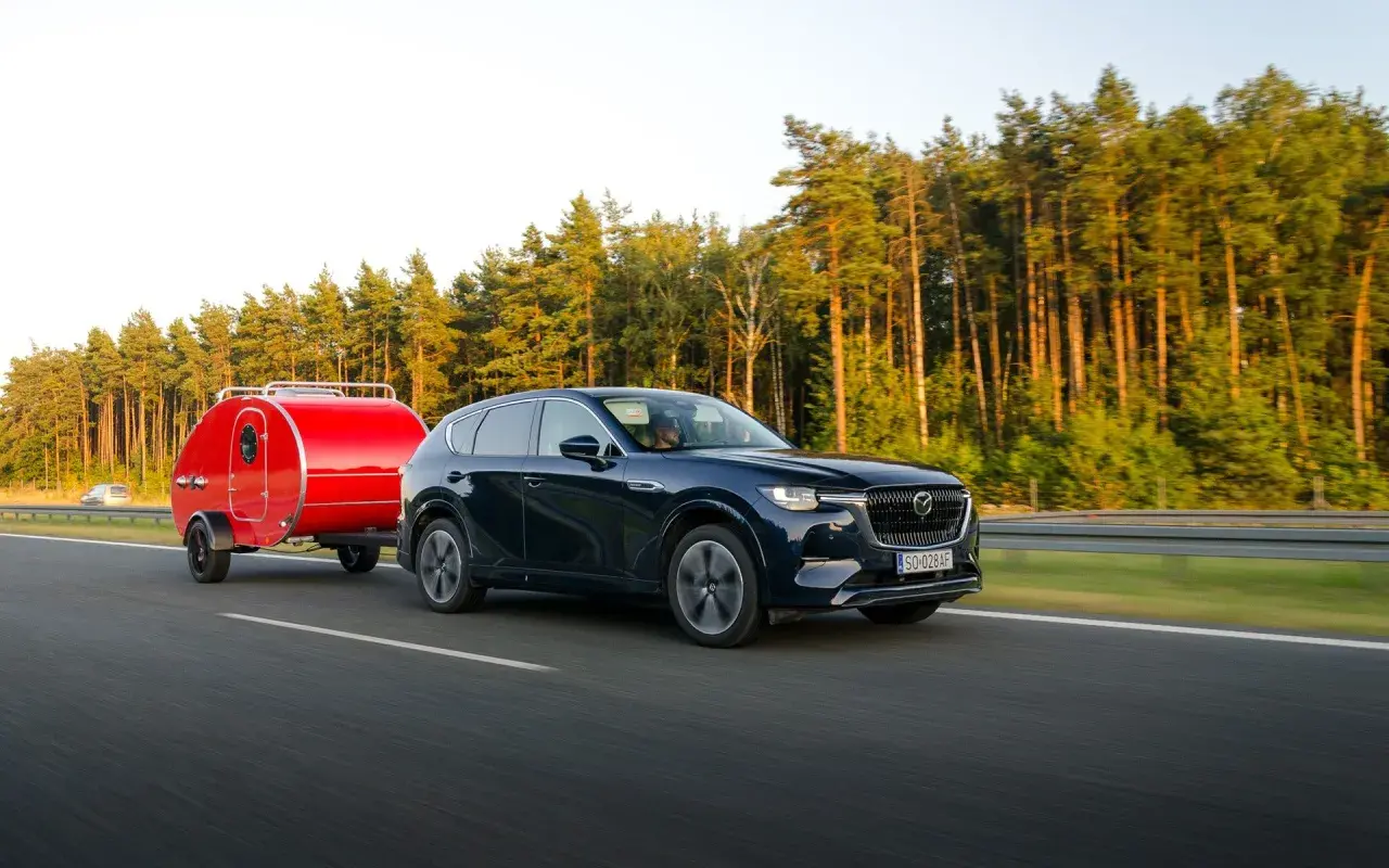 Ciemny SUV z czerwoną przyczepką typu teardrop jedzie po autostradzie. Zastanawiasz się, ile można jechać z przyczepką?