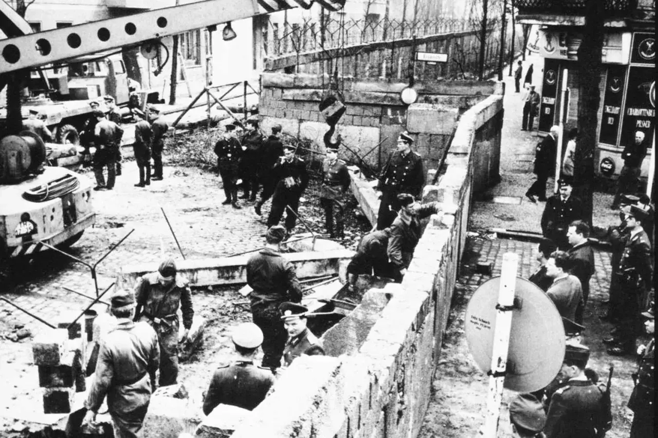 Militär och civila vid Berlinmuren, en scen som kan illustrera kalla kriget tidslinje. En kran lyfter bort delar av muren.