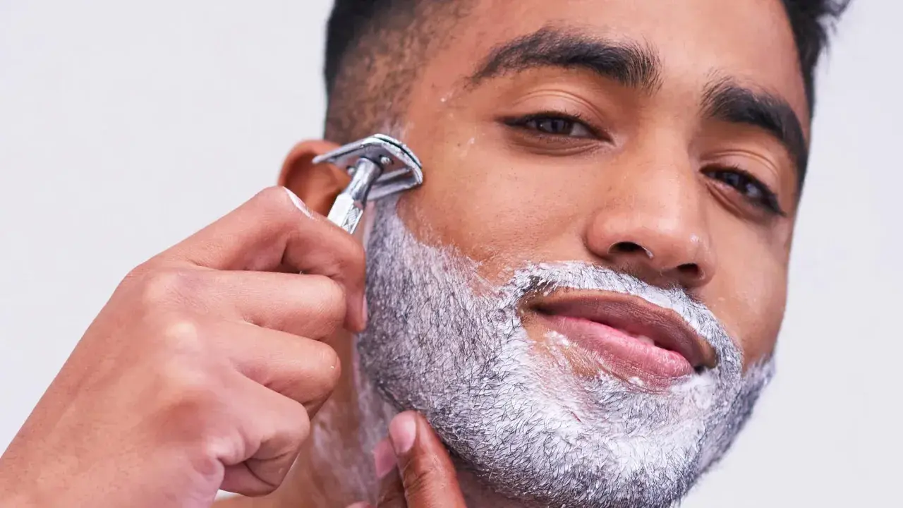 Uomo con schiuma da barba aggrappante prima della rasatura, mentre usa un rasoio di sicurezza.