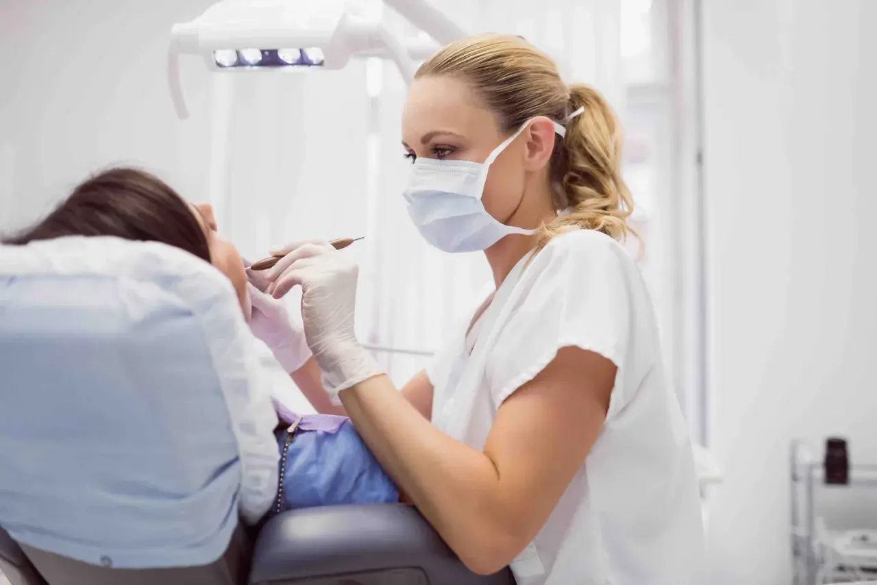 Dentista con mascherina esamina i denti di un paziente. La pulizia dei denti dura circa 30-60 minuti.