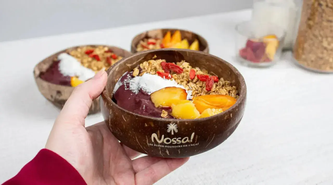 Une main tient un bol en noix de coco rempli d'un délicieux acai bowl, garni de fruits frais, de granola et de baies de goji.