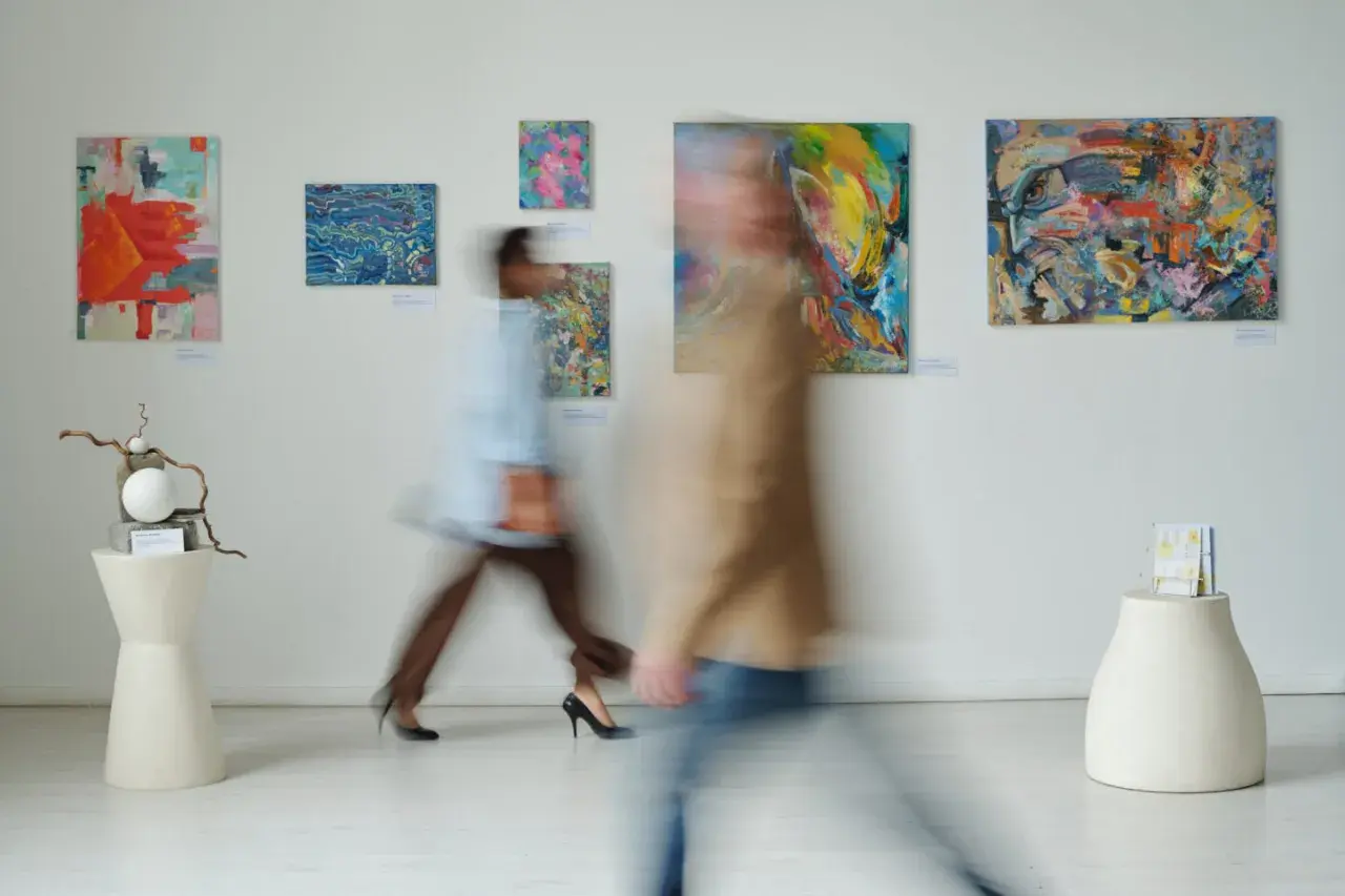 W galerii sztuki, gdzie obrazy zachęcają do kreatywności, jak w muzeum dla dzieci, dwie postacie w ruchu podziwiają abstrakcyjne dzieła.