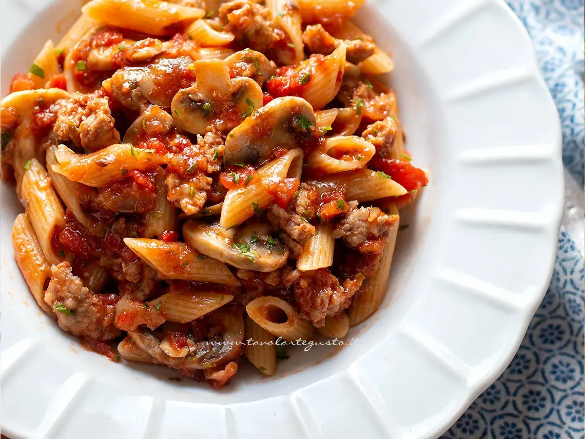Piatto di pasta alla boscaiola con penne, funghi, salsiccia e pomodoro, un classico saporito.