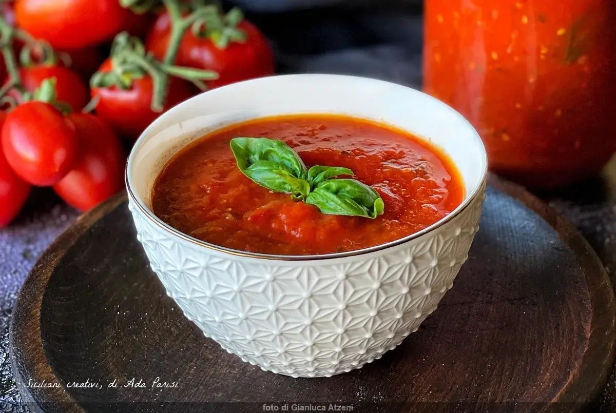 Una ciotola di salsa di pomodoro fatta in casa, guarnita con basilico fresco, con pomodori maturi sullo sfondo.