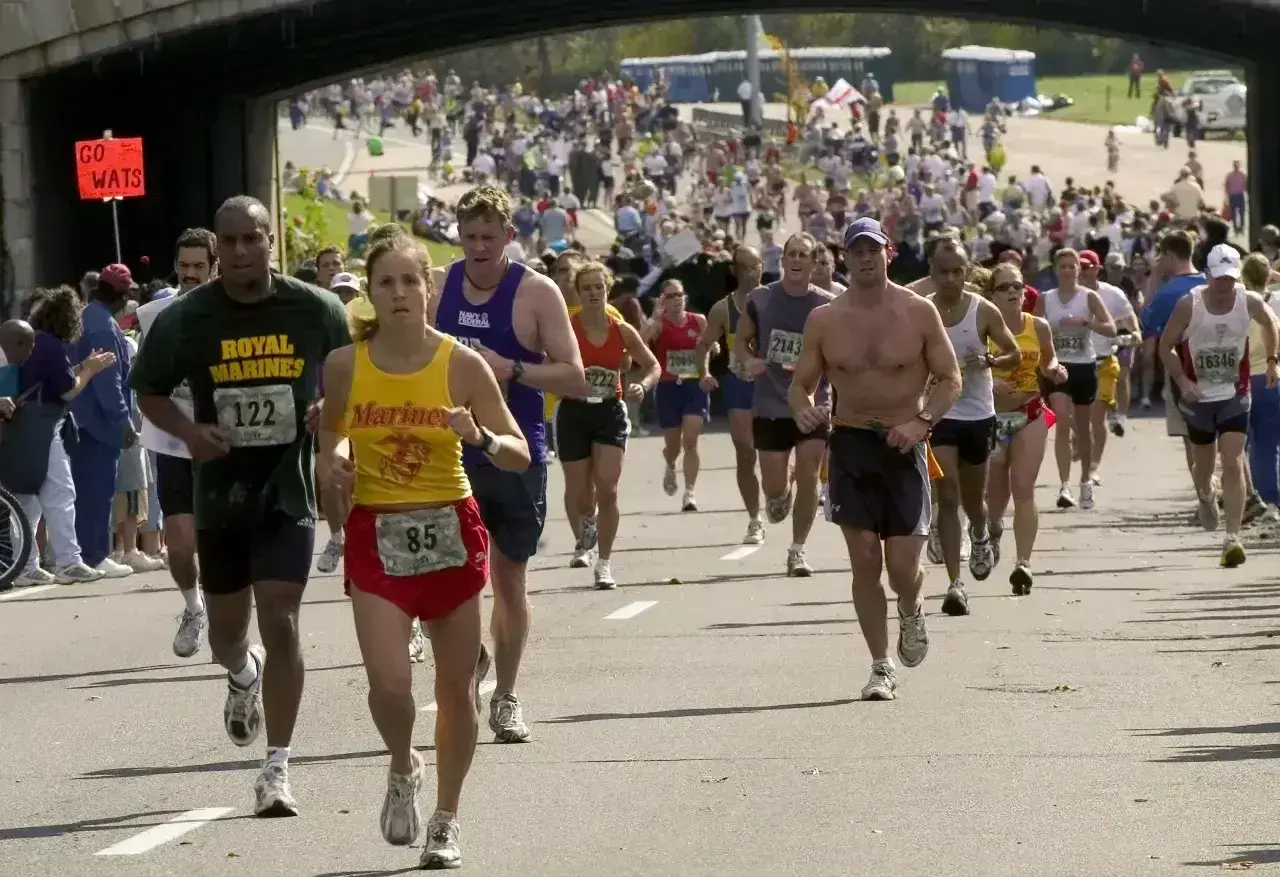 Uczestnicy biegną w maratonie, walcząc o jak najlepszy czas. Widać tłum biegaczy i kibiców.