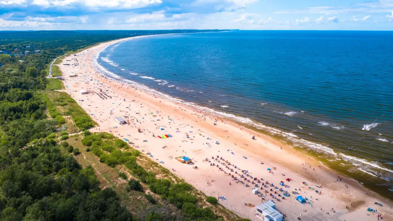 Słoneczne plaże nad morzem tętnią życiem. Tłumy plażowiczów odpoczywają na piasku, kąpią się w morzu i cieszą się wakacjami.