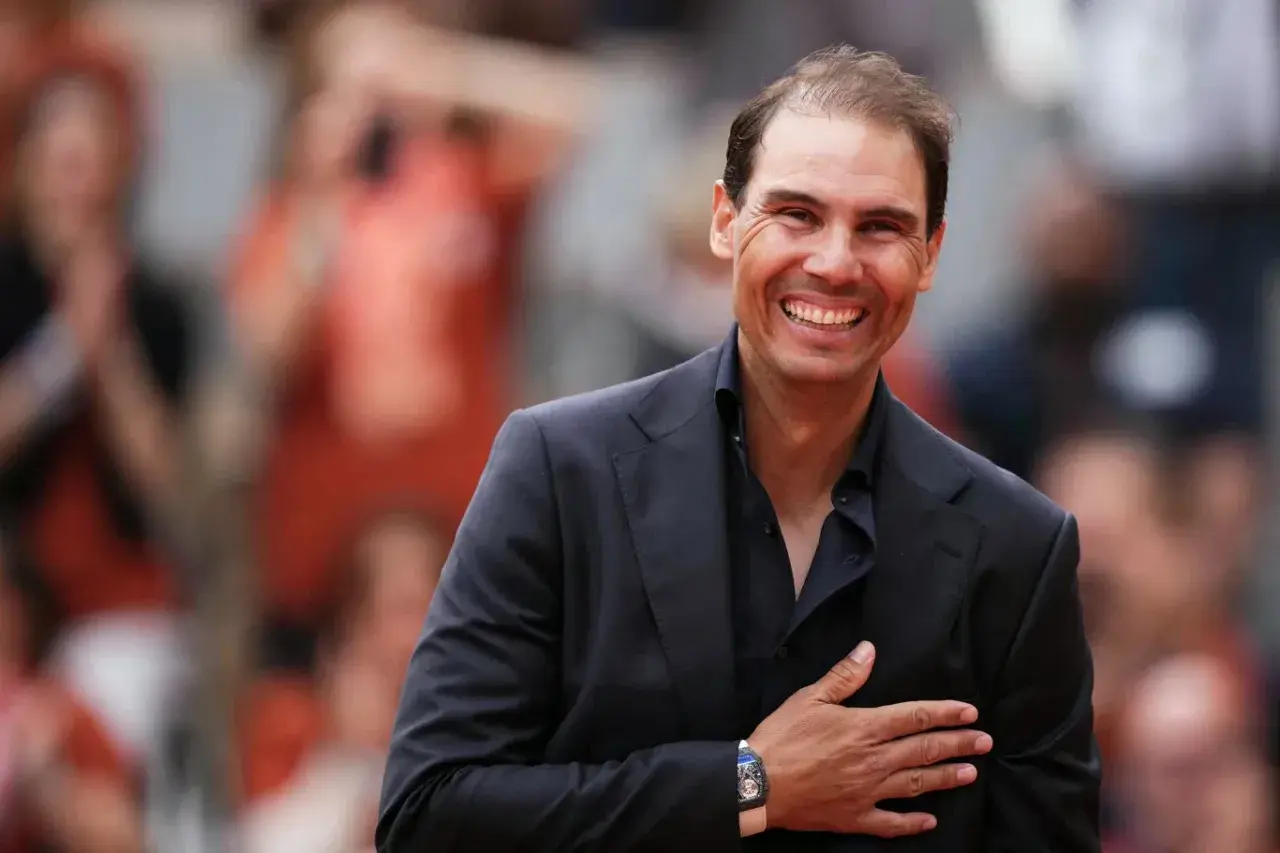 Uśmiechnięty Rafael Nadal, imię nadane temu słynnemu tenisisty, w czarnym garniturze i koszuli, z ręką na sercu.