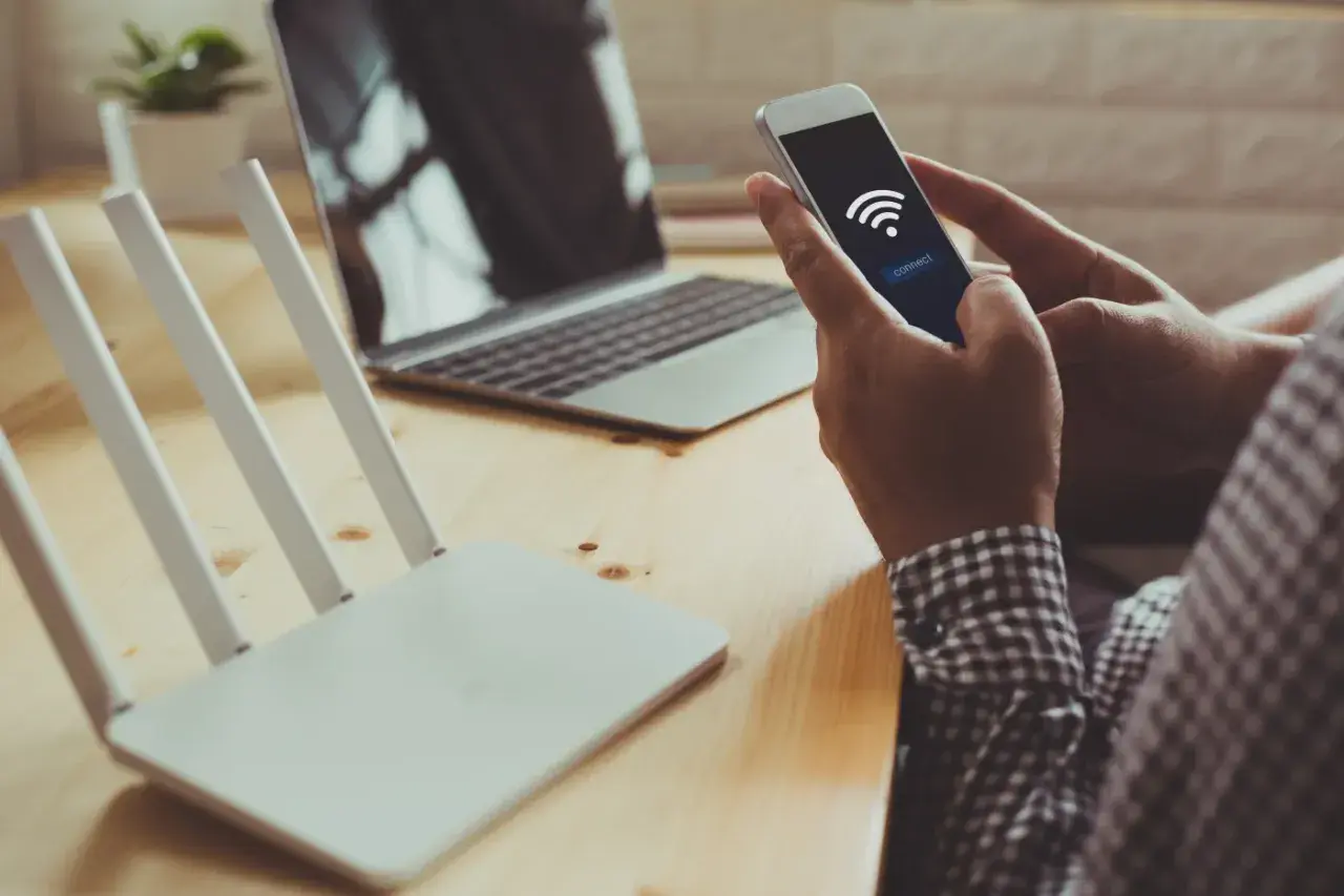 Dłoń trzyma smartfon z ikoną Wi-Fi i przyciskiem "connect", obok router i laptop. Szybkie połączenie dzięki wifi direct.