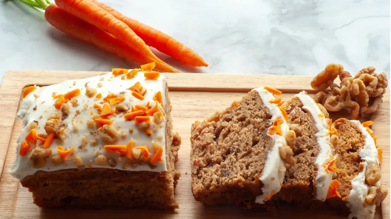 Saftiger karottenkuchen mit cremigem frosting, garniert mit geriebenen Karotten und Walnüssen. Daneben liegen frische Karotten und Nüsse.