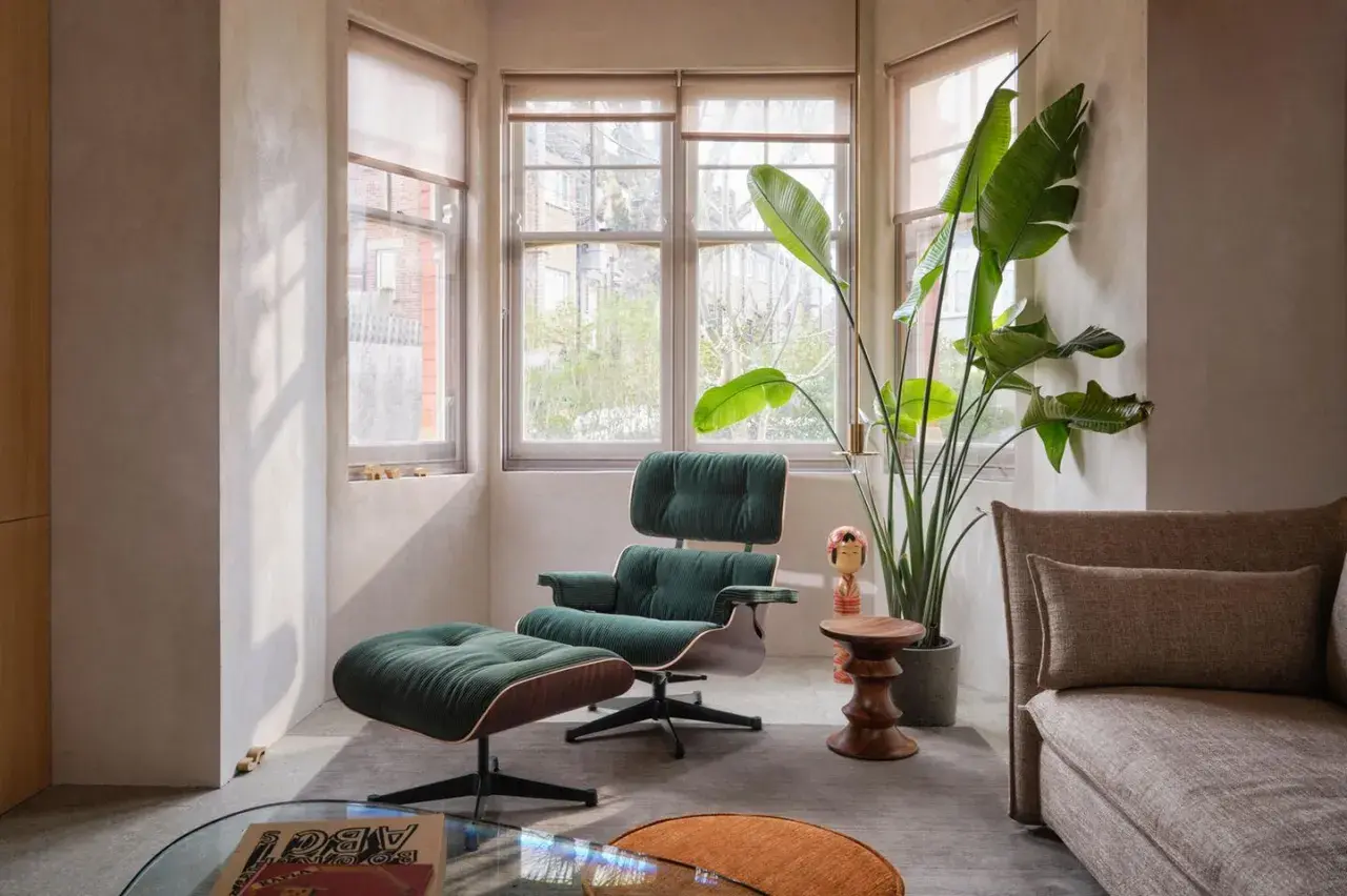 Ein gemütliches Mid-Century-Wohnzimmer mit einem grünen Sessel und Hocker, einer großen Zimmerpflanze und einem beigen Sofa.