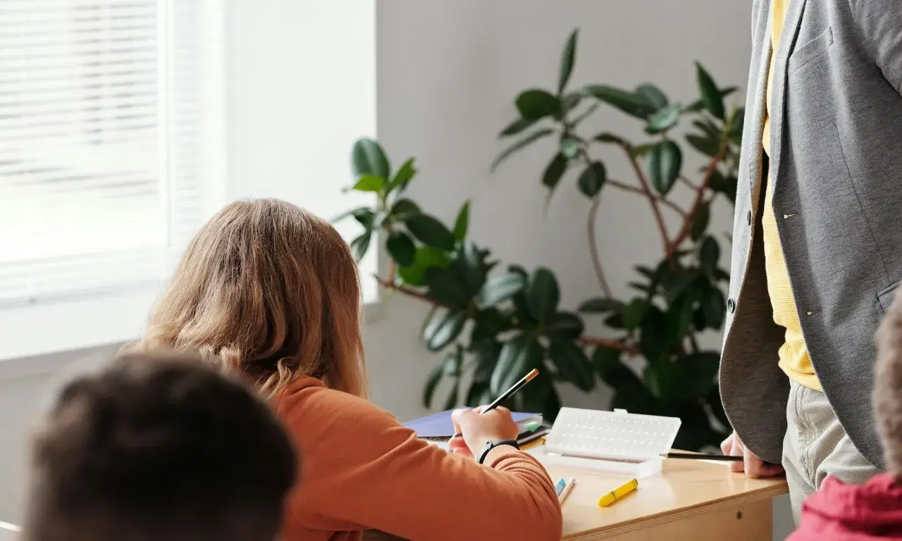 Ein Mädchen konzentriert sich auf seine Aufgaben während der Freiarbeit in der Grundschule. Ein Lehrer steht daneben.