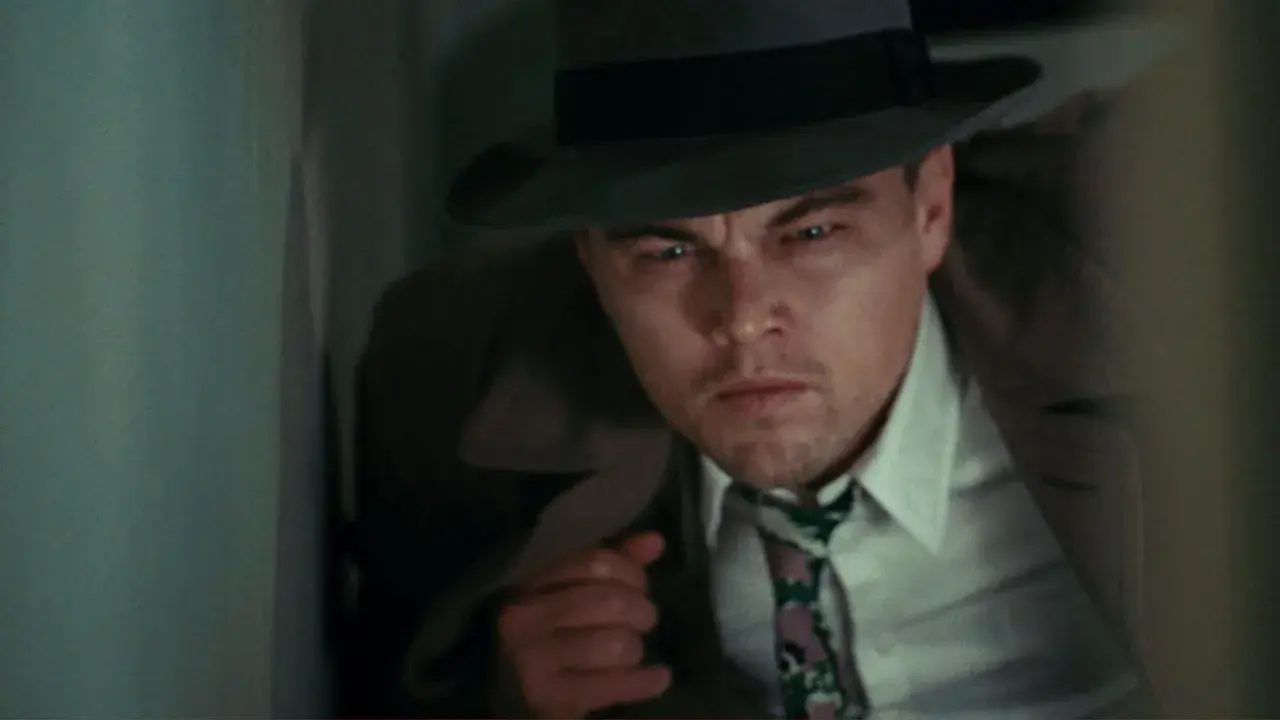 Leonardo DiCaprio, dans la distribution de Shutter Island, porte un chapeau et un trench-coat, l'air intense et méfiant.