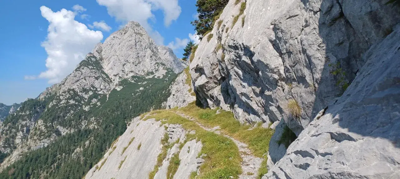 Ein schmaler Pfad schlängelt sich durch die felsige Landschaft der Karnischen Alpen. Im Hintergrund ragen schroffe Gipfel in den blauen Himmel.