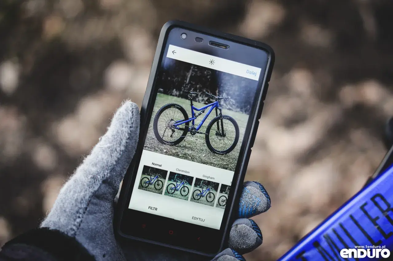 Rękawiczka trzyma smartfon z niebieskim rowerem na ekranie. Aplikacja oferuje filtry, jak w mapach rowerowych.