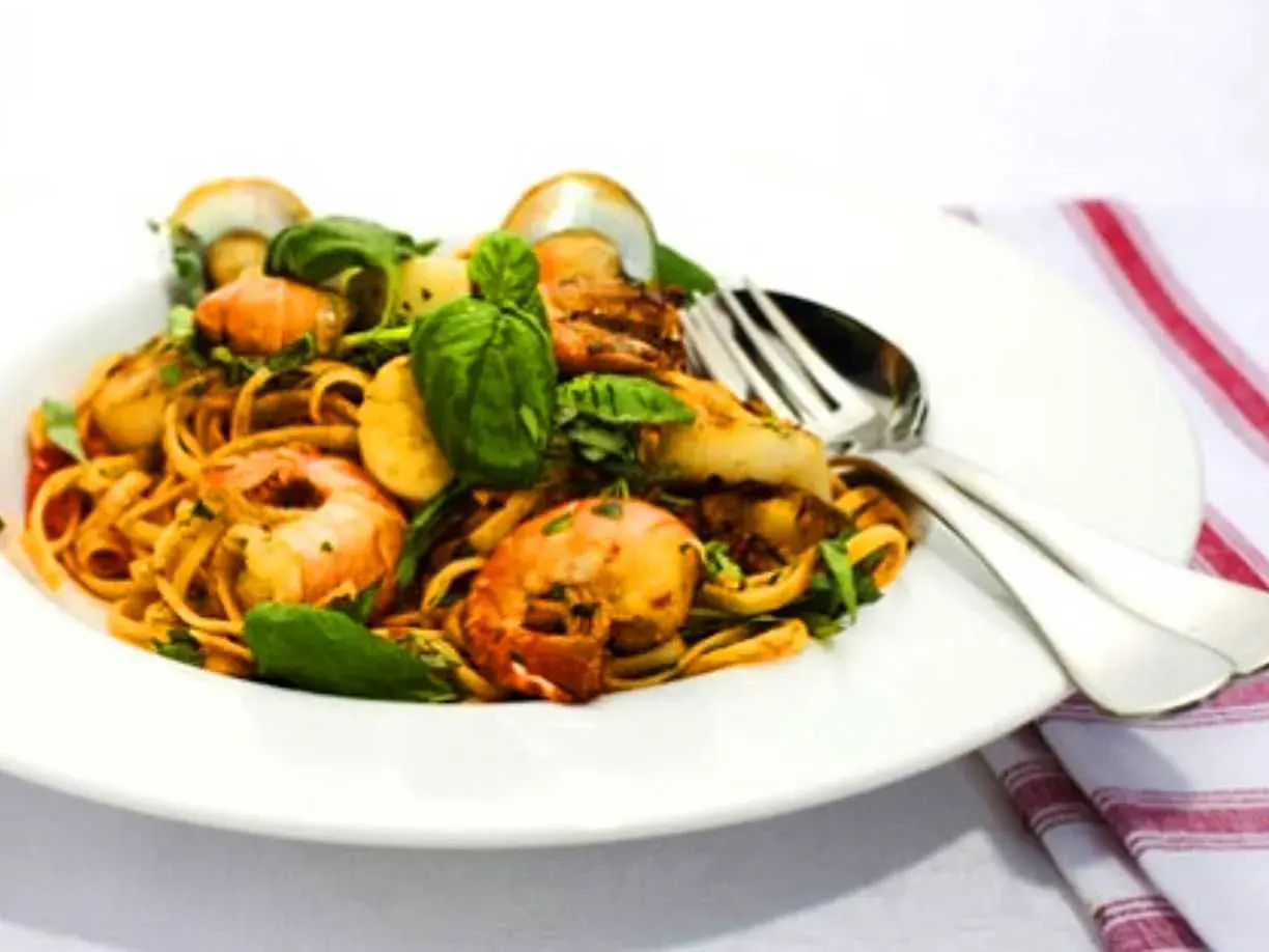 En tallrik med linguine frutti di mare, toppad med färska örter och serverad med bestick.