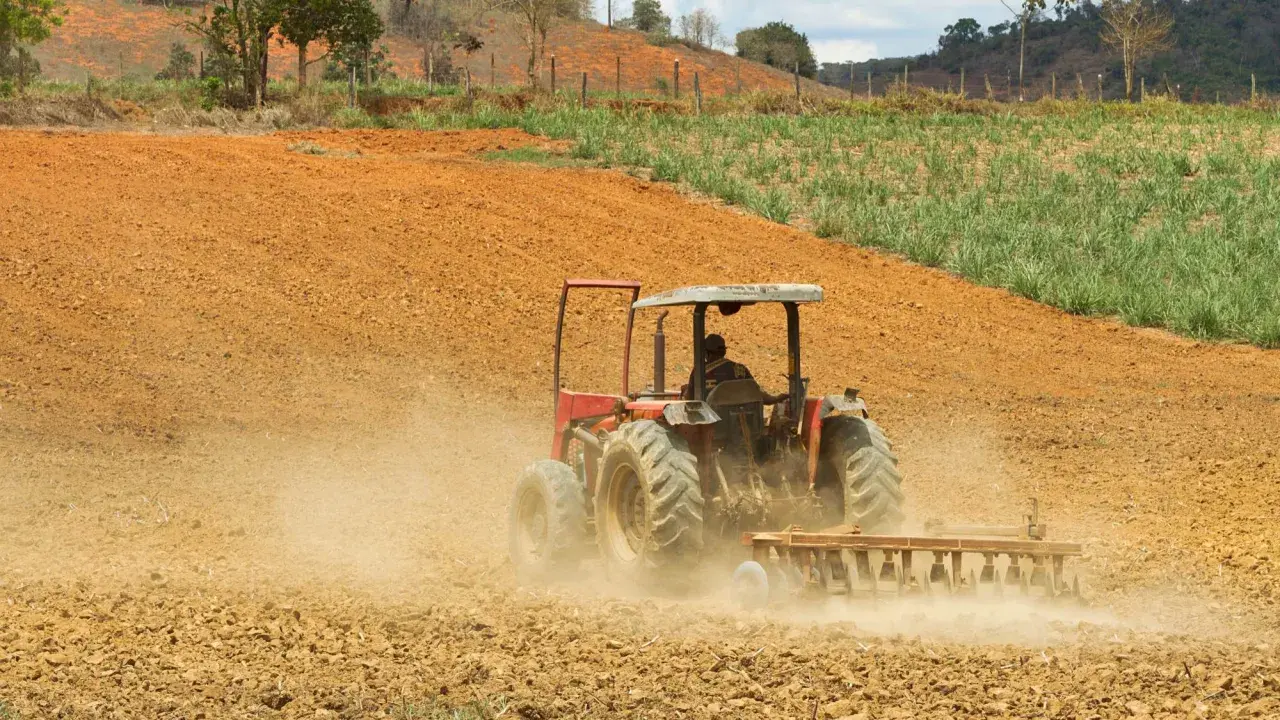 Czerwony traktor z pługiem orze ziemię, wzbijając kurz. To obraz rolnictwa regeneratywnego, przygotowującego glebę do nowego życia.