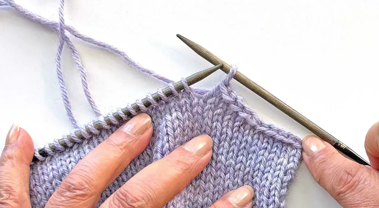 Close-up of hands sewing shoulder seams in knitting with lilac yarn and wooden needles.