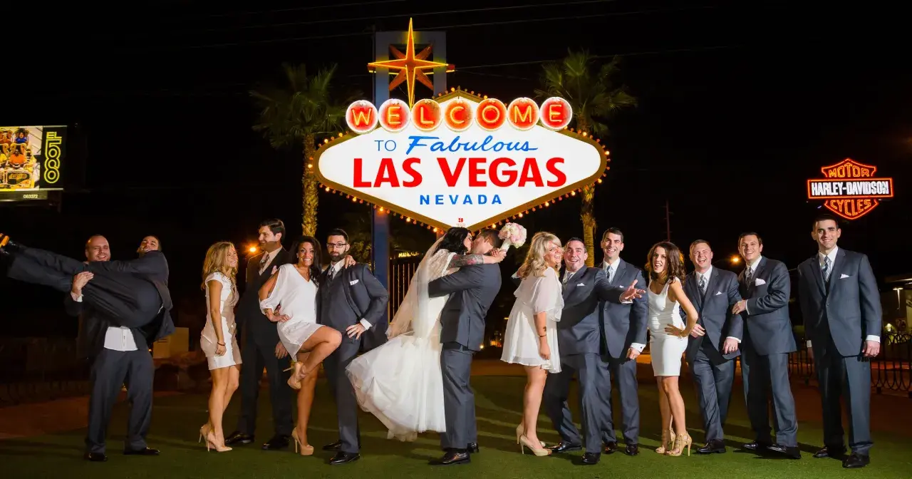 Ślub w Las Vegas jest ważny w Polsce? Para młoda całuje się pod neonem "Welcome to Fabulous Las Vegas", otoczona przez świadków.