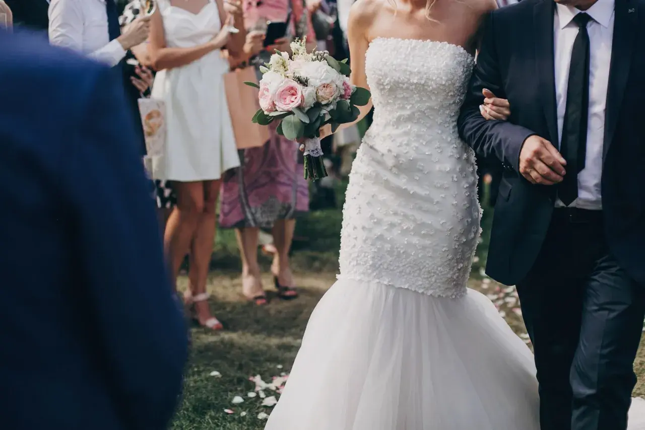Przepiękna suknia ślubna rybka, niczym syrena, podkreśla sylwetkę panny młodej. Bukiet róż i piwonii dopełnia jej ślubny look.