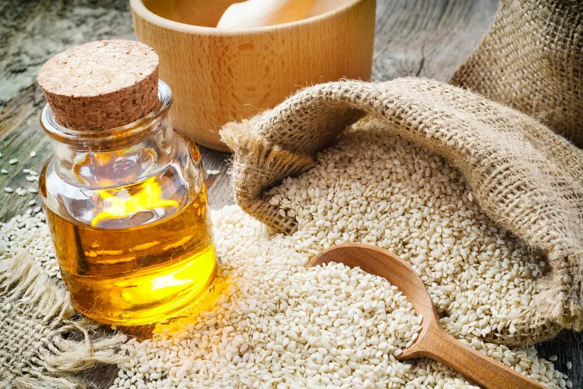 Olio di sesamo dorato in bottiglia, semi di sesamo in un sacco di juta e un cucchiaio di legno. Scopri le incredibili olio di sesamo proprietà.