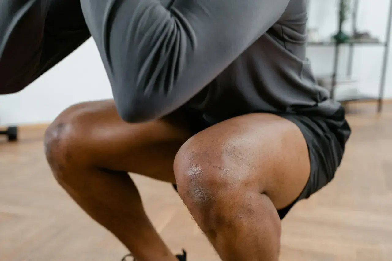 Ein Mann macht Kniebeugen, seine Knie sind gebeugt. Er hat leichte Narben auf dem rechten Knie, die auf frühere Schmerzen in der Kniekehle hindeuten könnten.
