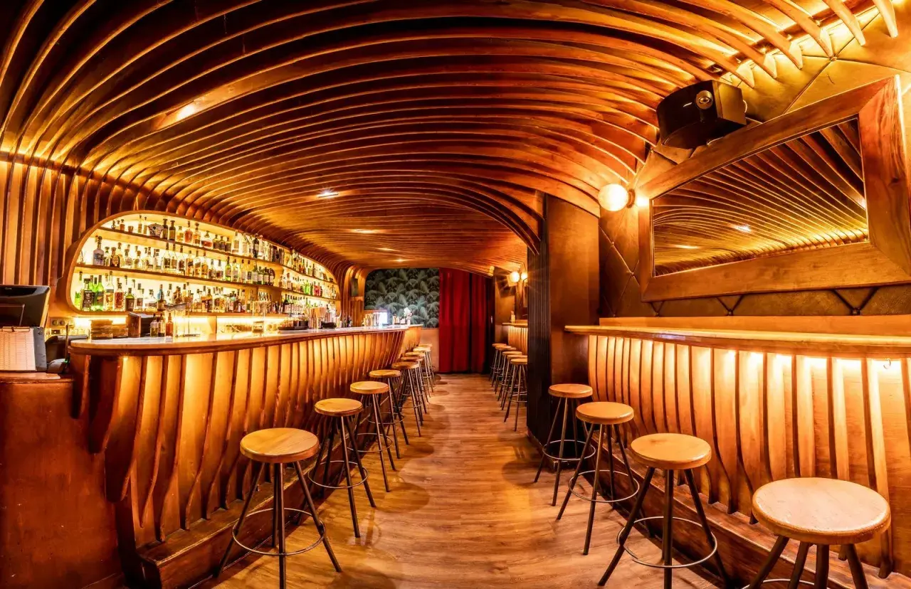 Bar de madera con estantes llenos de botellas, taburetes y un techo curvo. ¡Cosas curiosas que ver en Barcelona!