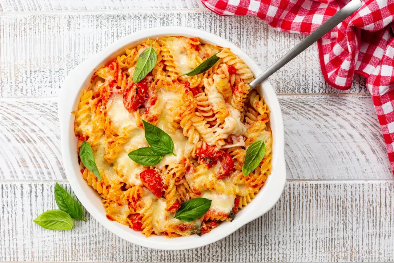 Un plat de pâtes fusilli gratinées avec une sauce tomate savoureuse et du fromage fondant, garni de feuilles de basilic frais.
