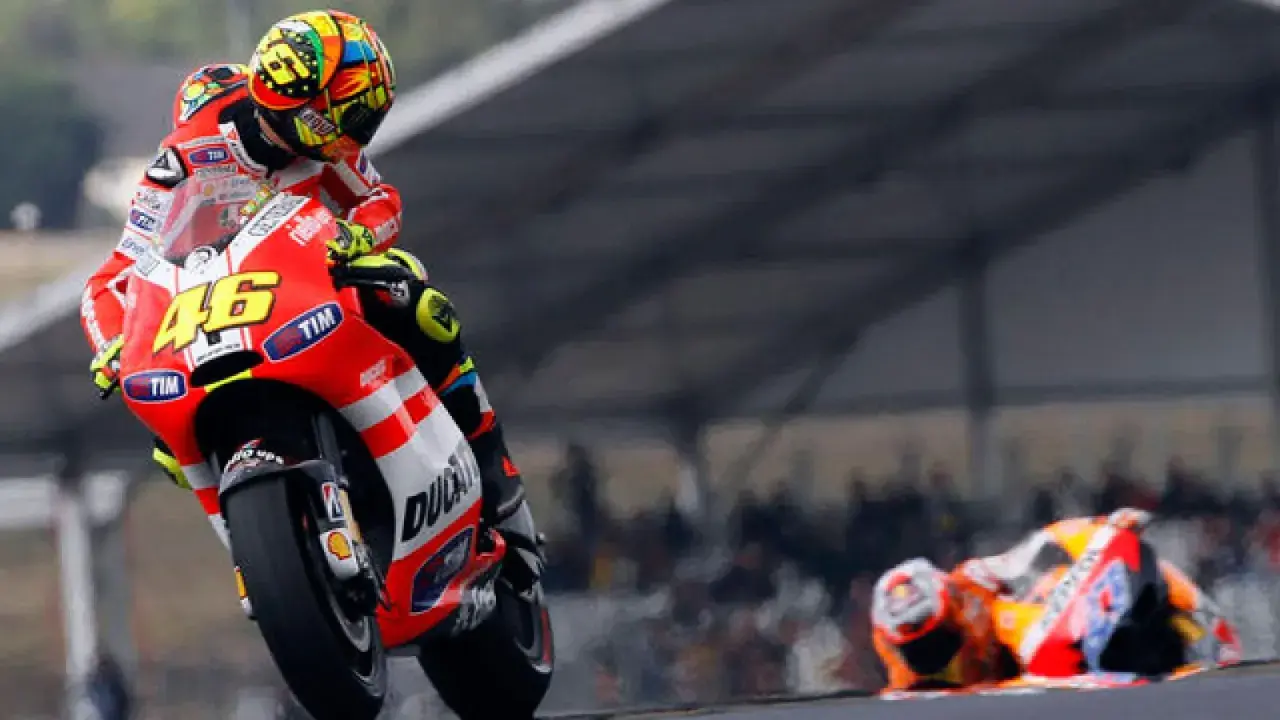 Valentino Rossi en su Ducati, número 46, inclinado en una curva. Otro piloto yace en el suelo.