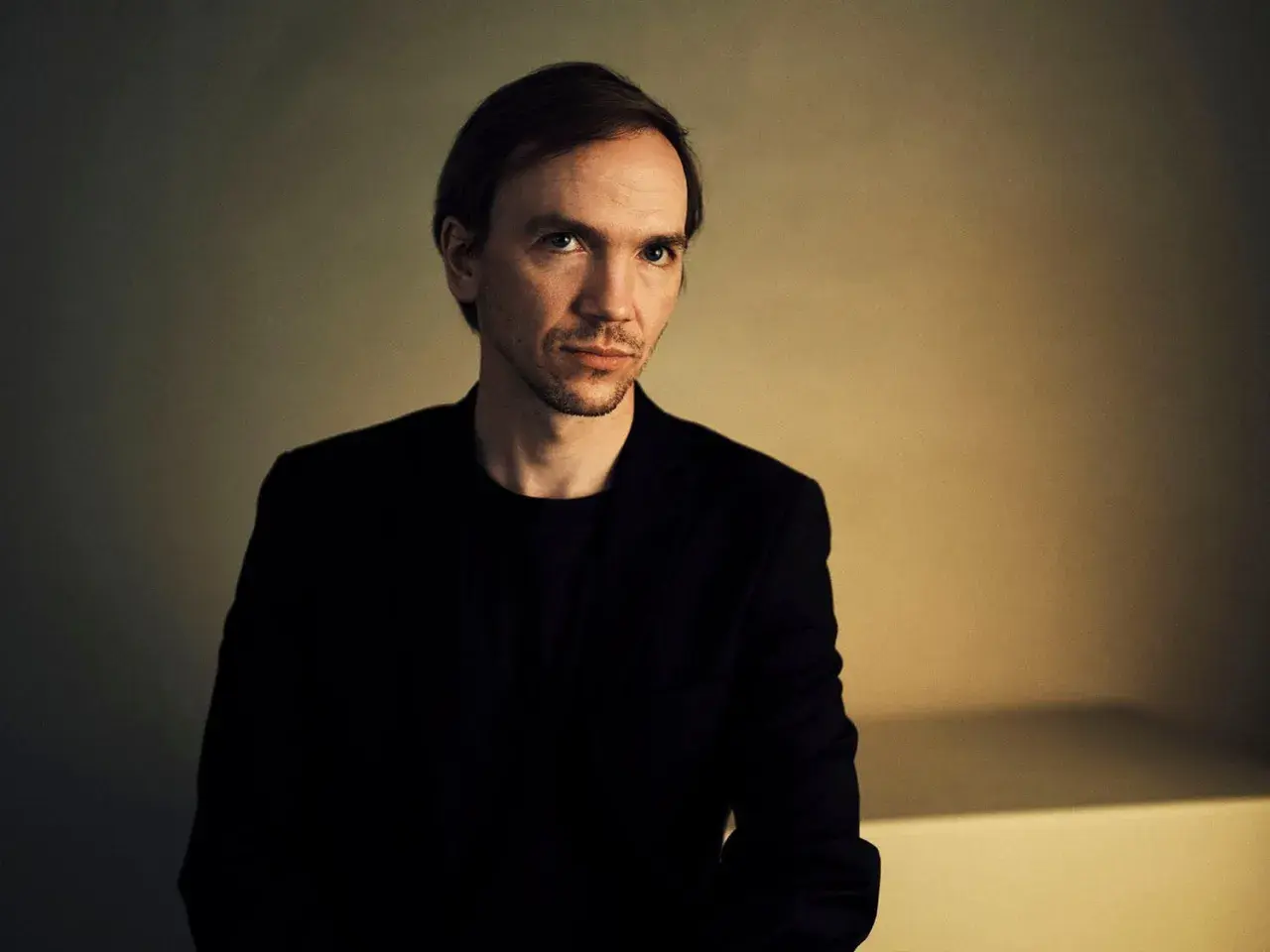 Portret Jana Komasy, reżysera znanych filmów. Jego spojrzenie sugeruje głębię i skupienie, jak w jego kinowych dziełach.
