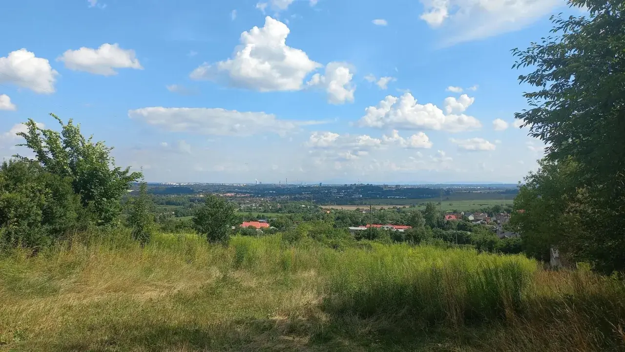 Widok z góry św. Doroty na zieloną dolinę z domami i miastem w oddali. Błękitne niebo z białymi chmurami.
