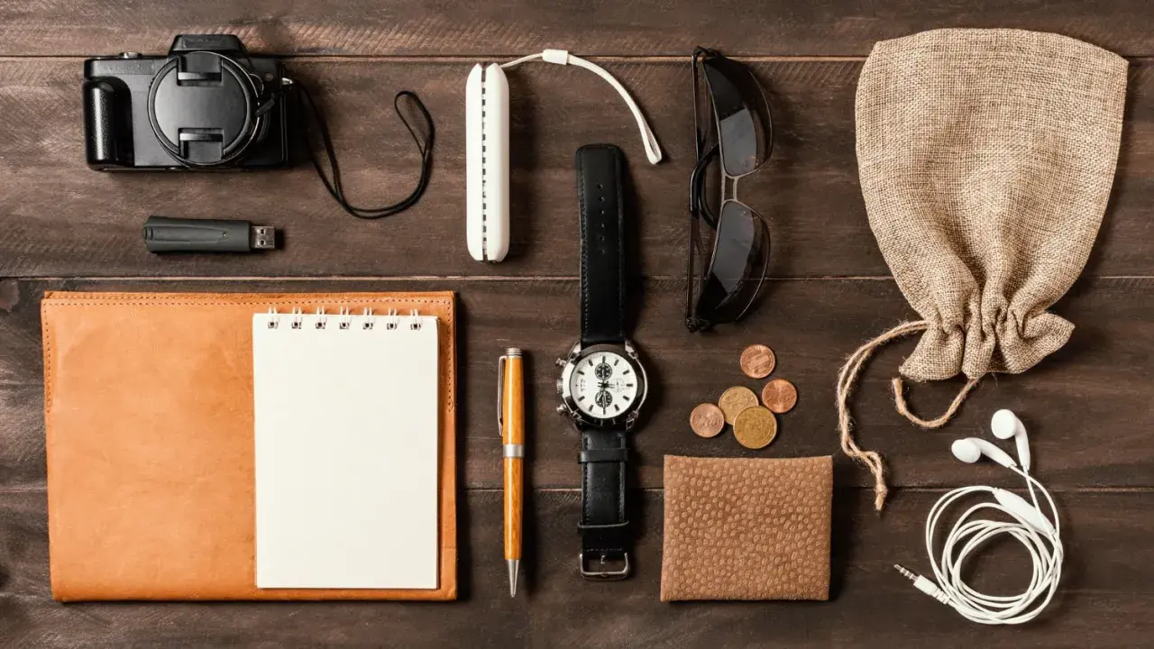 Zestaw EDC: aparat, pendrive, notes, długopis, zegarek, okulary, monety, portfel, słuchawki i woreczek.