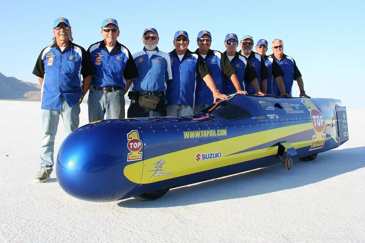 Ein Team steht stolz neben einem stromlinienförmigen Fahrzeug, das aussieht, als wäre es das schnellste Motorrad der Welt.