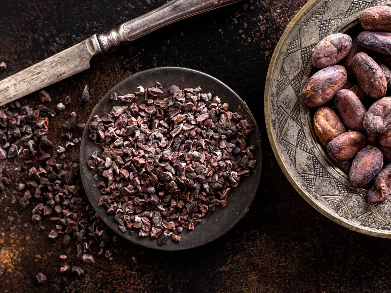 Un coltello d'argento accanto a una ciotola di **semi di cacao** tritati e un piatto decorato con semi di cacao interi.