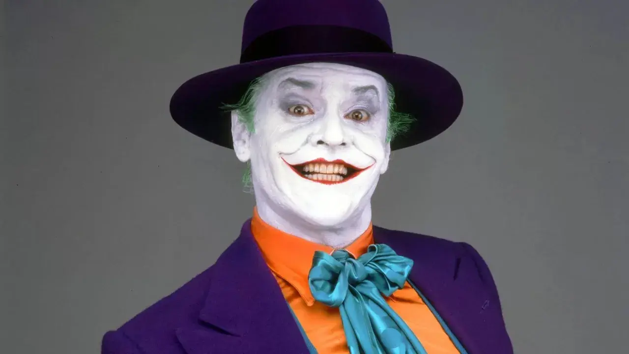 Jack Nicholson nel suo iconico ruolo di Joker, primo film, con trucco bianco, capelli verdi e cappello viola.