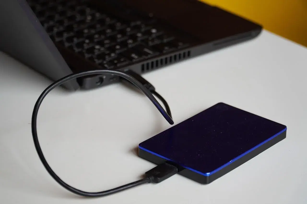 Un disque dur externe bleu est connecté à un ordinateur portable. Un guide pour comment choisir son disque dur externe.