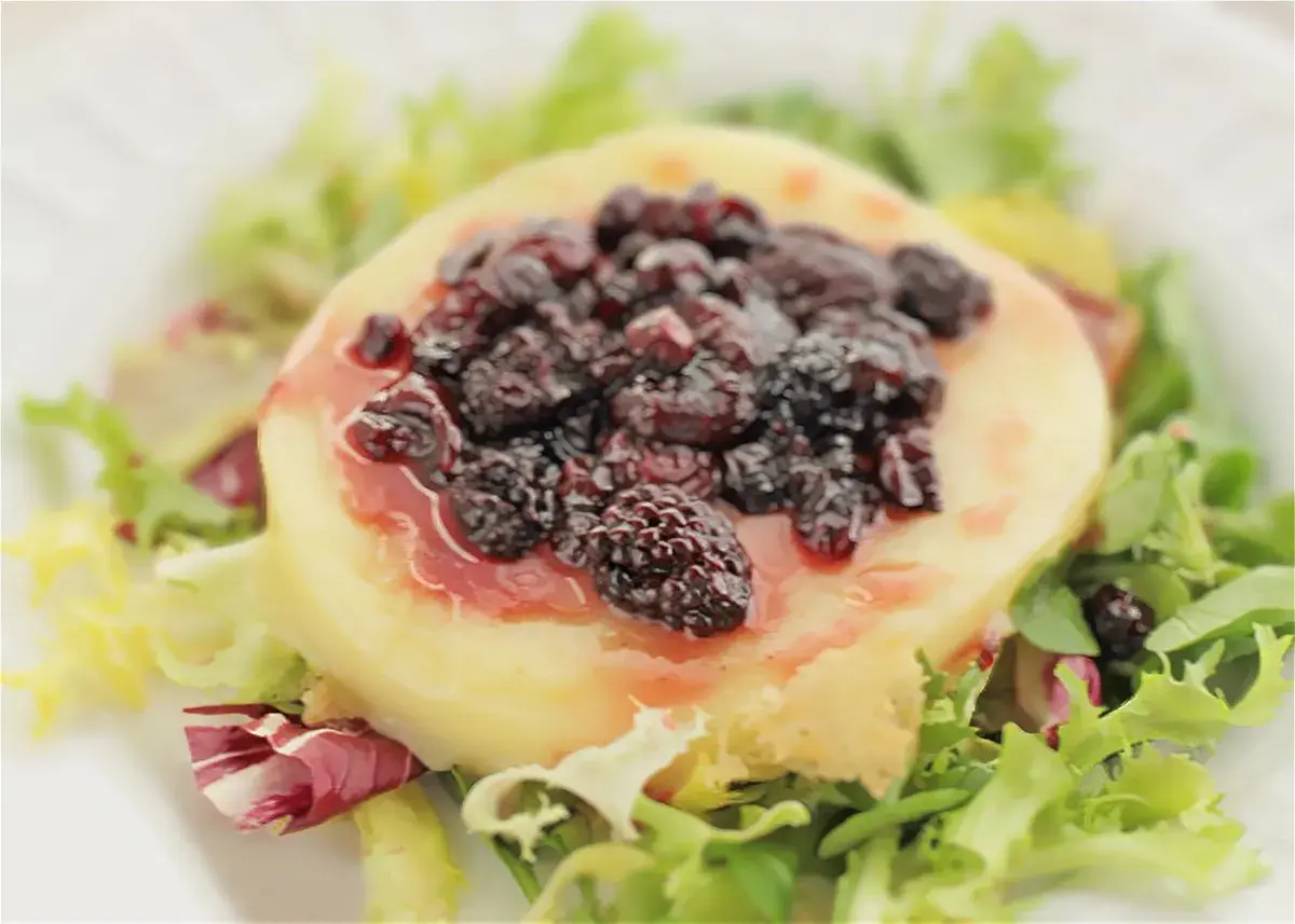Provolone a la plancha cubierto con moras y salsa, servido sobre una cama de lechugas mixtas.