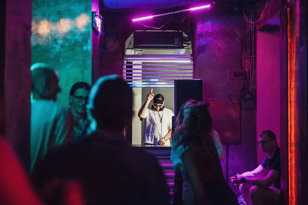DJ w klubie, podniesiony palec, neonowe światła, różowy sober tekst.