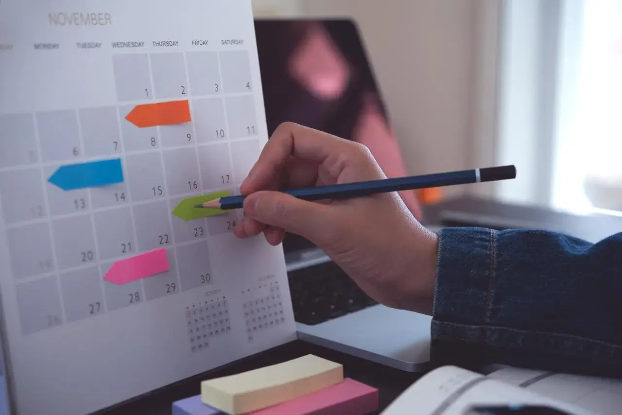 Kalender med färgglada post-it-lappar markerar viktiga datum. En hand med en penna planerar för bokslut enskild firma.